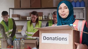 A Muslim woman volunteer in a hijab holds a donation box and smiles. Food crisis. Charity in Ramadan