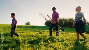 Side view: A family of farmers with a small son go together to plant a tree. Bear the apple tree seedlings, shovel and watering pad. Steadicam shot, side view