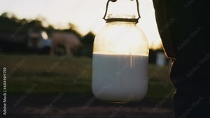 Plastic milk jar in woman hands on farm. Milkmaid farmer carrying raw milk on field in village, close-up. Natural home production dairy products for healthy nutrition. Keeping livestock on farmland.