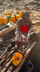 A Gambue woman from Angola drawing water from a well is caught in a typical, communal scene: dressed in colorful fabrics, she bends over the earthen or stone well, uses a bucket attached to a rope, and lifts it with strength and skill. The water is poured into gourds or jerrycans, which she then carries home, symbolizing her essential role in family life and the organization of the village. #inspirationofafrica | Quim Fàbregas - Fotografía y Viajes.