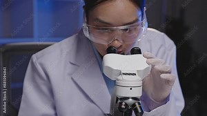 Scientist in lab with safety gear examining samples through a microscope in modern setting. Professional research and scientific investigation