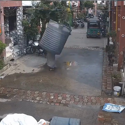 A shocking video capturing the moment a woman narrowly escaped death after a water tank plummeted from above is gaining widespread attention on social media. The brief clip, shared on a microblogging site, shows a woman dressed in a saree casually stepping out of her house while eating an apple. Mere seconds later, a large water tank unexpectedly crashes down, hitting her and knocking her to the ground. Fortunately, despite the close call, the woman emerged from the incident unharmed. #ViralVide