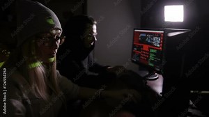 Male and female hackers working on computers with data code on display screens in a dark room. HD.