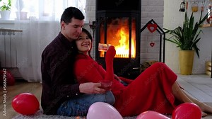 Man and woman in love date at home are sitting near the fireplace stove with a burning fire on a cozy rug. Valentine's Day, happy couple, love story, relationships