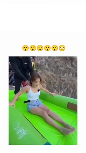 viral memes on Instagram: "The post shares an 11-second video of a woman screaming as she slides at high speed down a bright green inflatable waterslide built along a steep cliff overlooking a river valley in a mountainous area, ending with a double-bounce splash into a blue landing pad below. Authored by Rwandan influencer @inkwakuzi_ , a self-described animal health scientist, the clip's shock emojis underscore its intent as thrilling entertainment, quickly garnering 86,000 views, 16 likes, an