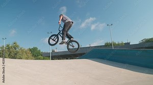 A professional cyclist rides and performs tricks on bmx. Beautiful stunts and bike jumps in the park on a concrete platform with obstacles. BMX.
