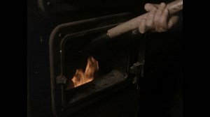 1950s: Man shovels coal into stove, flames rise, man closes door.