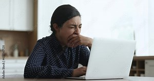 Tired with on-line work yawning young Indian female sits at desk with laptop, doing telework at home, feels unmotivated or too exhausted, information or study overloaded need rest or more motivation