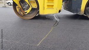 A large asphalt road roller, a vibrating roller that moves and compresses the freshly laid asphalt base, road infrastructure reconstruction