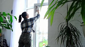 Woman manually washes the window of the house with a rag with spray cleaner and mop inside the interior with white curtains. Restoring order and cleanliness in the spring, cleaning servise