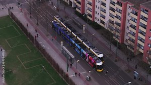 Aerial view of Berlin's tramway public transportation, operating in a city station surrounded by buildings, pedestrians crossing the street, a park and residential buildings