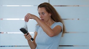 Woman brushing hair with hairbrush, worrying about hair loss shedding or bad condition. Upset woman hair loss.