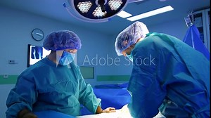 Female medics perform operation in modern surgery room. Surgeon works under the bright lamp.