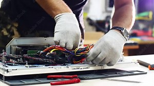 Technician works in service center. Repairman detaches power supply repairs computer monoblock in workshop. He disconnects wires, takes out and puts detail on table, continues to diagnose monitor.