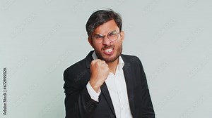 Aggressive angry Indian businessman trying to fight at camera, shaking fist, boxing with expression, punishment, threaten, bullying, abuse, mad fury. Arabian man guy isolated on gray studio background