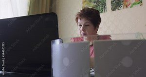 Senior lady using computer in home office, middle aged woman grandma working in room house, older people and modern tech concept. 60s elder woman holds mobile phone checking app, reading news at home.