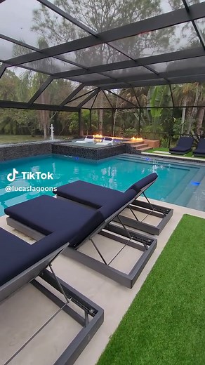 We design and build some insane modern pools. This backyard features an elevated sun shelf with ledge loungers, a swim-up bar, fire features, an outdoor kitchen, a sunken living area, a fountain wall, and a screened enclosure. #insanepools #lucaslagoons #modern