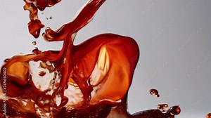 Liquid dance in slow motion, an elegant ballet of amber drops. A caramel-colored liquid, possibly coffee or tea, poured or splashed on a white background, highlighting its rich color