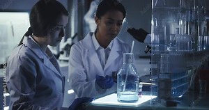 Young female scientists working after hours. Using microscope in futuristic laboratory