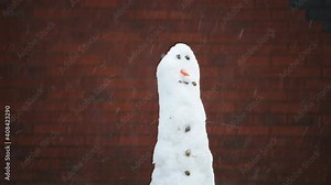 4k Snowman in the garden as it's snowing in front of a brick wall