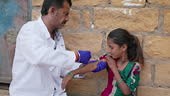 Male doctor vaccinating young Indian girl in small village,...