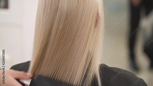 A close up back view of blonde's hair brushed by a vent hair brush to length. The camera slowly moves top down.