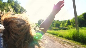 Woman leaning out of car window and holding her hand out while riding through countryside road. Girl looking out from window of moving auto and enjoying journey. Travel or road trip concept. Slow mo