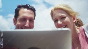 Couple on beach with computer tablet laughing at what they see on the screen