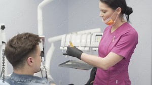 Female Dentist in Her Purple Uniform and Black Gloves Explains Teeths Phisiognomy with Artificial Model to Male Patent. Some Dental Instruments in Background