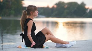 Lonely woman sitting on lake side on warm evening. Solitude and relaxation concept