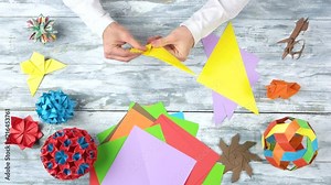 Hands making origami figure, close up. Art of origami, flat lay, top view. Wooden desk surface. Stock Video
