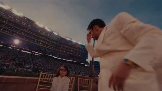 FOUND WANTING on Instagram: "My favorite segment from Bad Bunny’s Super Bowl halftime show (2026) The sequence is filmed with a wide-angle wandering camera technique that follows Benito as he navigates around a vibrant wedding party, mock-directing the camera to follow him through the crowd. In the middle of his performance, he takes a moment to wake up a kid who is asleep on a makeshift bed of three chairs, paying homage to a universal experience within the Latino community of the ever-present 