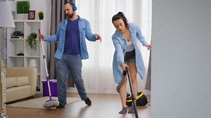 Cheerful man dancing while cleaning the house together with his wife. Happy dancing singing couple cleaning apartment, household and housekeeping, vaccum and mop, clean-up the house