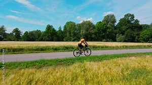 Cyclist training on bicycle. Male sportsman wearing cycling uniform and helmet riding road bike on countryside path near blooming agricultural fields. Active outdoor sports