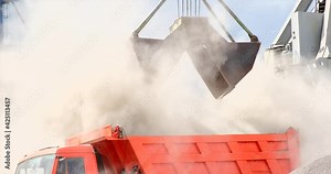 Grapple crane unloading cement clinker from ship to truck in port. Grab is discharging bulk cargo from a hold of cargo ship, causing dust in atmosphere. Loading in Harbor outdoors. Logistics