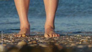 Pleasure of sand between toes. Girl standing on edge of water at beach wriggles toes in warm sand in soft evening light