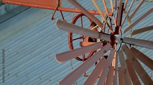 Rust coloured spinning windmill with tin roofs in the background. locked off, close up