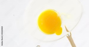 Popping and piercing egg yolk.Close-up Slow motion. Spilling egg yolk. white background.