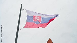 Slow motion of flag of Slovakia flying on the wind in front of Parliament. Waving flag of Slovak Republic on flagpole. White, blue and red colors. Slovakia's national coat of arms.