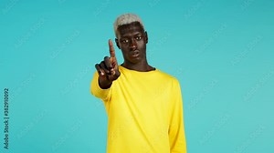 African man in yellow disapproving with no finger sign make negation gesture. Denying, Rejecting, Disagree, Portrait of guy on blue background.