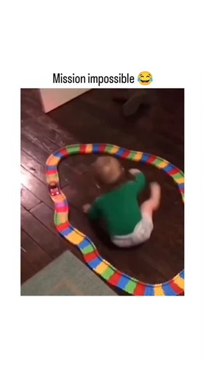 @meme.chillipop on Instagram: "Instagram features a 19-second video of a baby in a green onesie comically crawling, rolling, and struggling to navigate inside a closed loop of colorful toy train tracks on the floor, set to upbeat music, captioned "Mission impossible " to evoke action movie antics. Posted by , an account specializing in lighthearted, non-toxic comedy clips like pranks and animal videos, the post garnered over 23,000 likes and 772,000 views within 24 hours, indicating strong appea