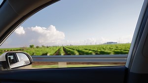 View from the side window of a car driving fast along the highway during a beautiful sky and field. Travel trip and adventure concept.