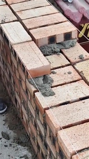 Placing brick blocks on fresh mortar and aligning rows carefully to build wall layer