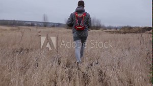 Traveling man walking in nature. Calm male with backpack strolling through field in cloudy weather