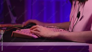 Close-up of young woman playing computer game. Stock footage. Gamer plays on computer by pressing keyboard and mouse. Girl plays computer games with keyboard
