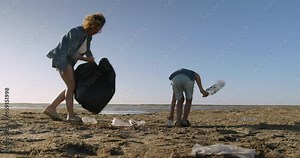 Female volunteer with kid collects garbage on beach. Pollution of nature with plastic waste. Clean environment. Child with volunteer collect plastic garbage in garbage bags. Ecology, eco activism