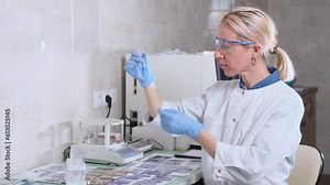 A female laboratory assistant examines the liquid in a test tube and looks at it carefully. A female research scientist conducts an experiment in the laboratory.