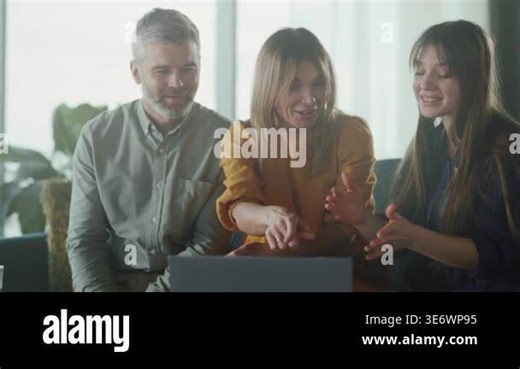 caucasian family watching laptop reveal, parents and adult daughter gather on bright living room sofa, excited Stock Video Footage - Alamy