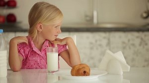 Cheerful little girl sitting at kitchen table drinking milk and smiling