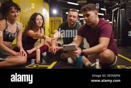 Group of friends sits on the floor of a fitness center discussing their exercise plans. They review their goals and share ideas for group workouts in a casual and friendly setting Stock Video Footage - Alamy